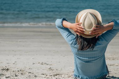 Kumsalda oturup denize bakan rahat genç bir kadın.