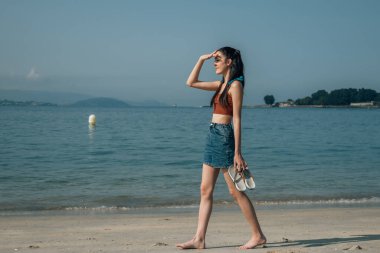 Genç bir kadın sahilde ufku tarıyor.