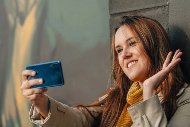 Akıllı telefonlu genç bir kadın sokakta selam yolluyor.