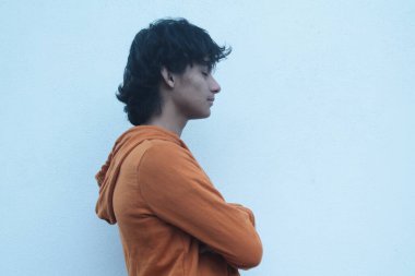 Duvarda kollarını kavuşturmuş genç bir adam.