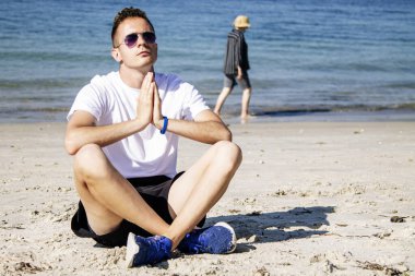 Genç adam plajda meditasyon ya da yoga egzersizleri yapıyor.