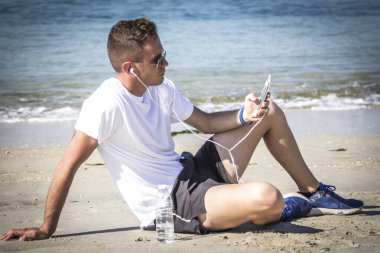 Rahatlamış genç adam plajda kulaklıklarıyla müzik dinliyor.