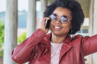 Genç Afro kadın sokakta telefonla konuşuyor.