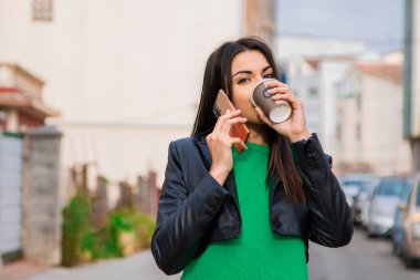 Sokakta kahve ve telefonla dolaşan Latin bir kadın.