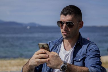 Cep telefonlu rahat genç adam plaj barında kahve içiyor.