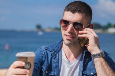 Cep telefonlu rahat genç adam plaj barında kahve içiyor.