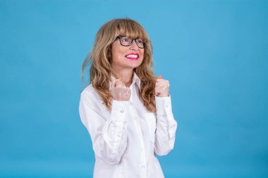 Mavi arka planda başarılı bir jest yapmış olgun bir kadın.