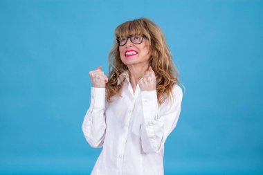 Mavi arka planda başarılı bir jest yapmış olgun bir kadın.