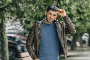 Deri ceketli genç adam sonbaharda parkta yürüyor.