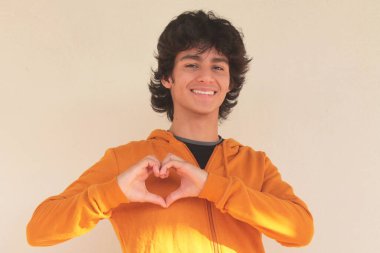 Gülümseyen genç latin adam elleriyle kalp yapıyor.