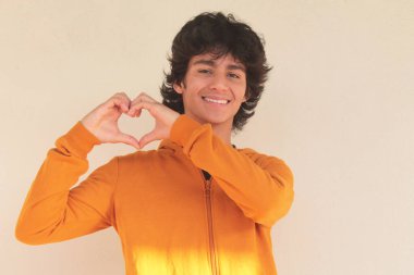 Latin kökenli genç bir adam elleriyle kalp yapıyor.