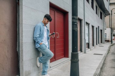 Sokak duvarında cep telefonuyla sohbet eden sıradan bir genç.