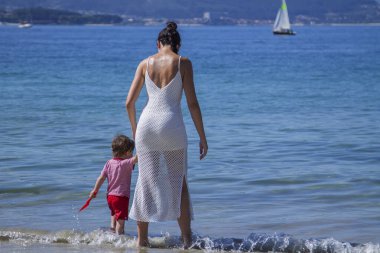 Anne ve oğlu el ele kumsalda yürüyor.