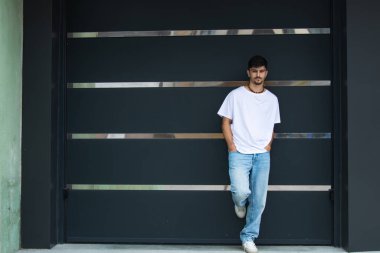 Duvarın karşısında duran şık bir gencin ön görüntüsü.