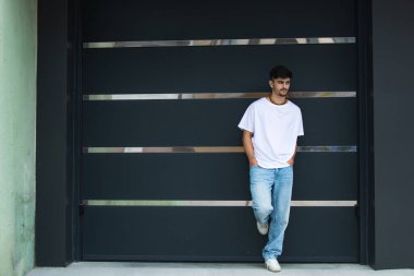 Front view of a fashionable young man standing against the wall clipart