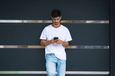 Duvardaki genç adam cep telefonu kullanıyor.