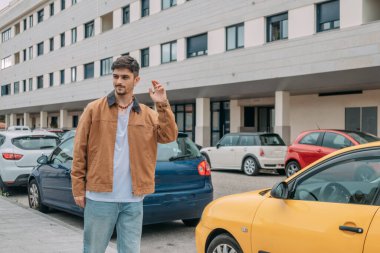 Sonbaharda şehirde yürüyen ve el sallayan ceketli genç adam.