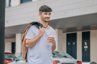 Şehir caddesinde elinde kağıt bardak tutan ceketli yakışıklı bir adam.