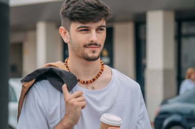 Şehir caddesinde elinde kağıt bardak tutan ceketli yakışıklı bir adam.