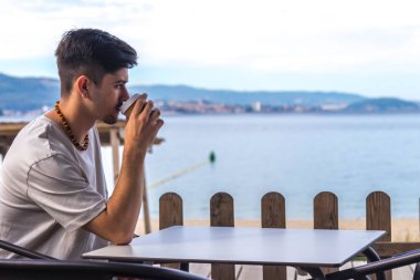 Plaj barındaki genç adam rahatlamış bir kahve içiyor.