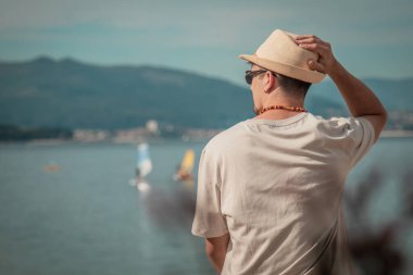 Genç adam sahilde oturmuş denize bakıyor.