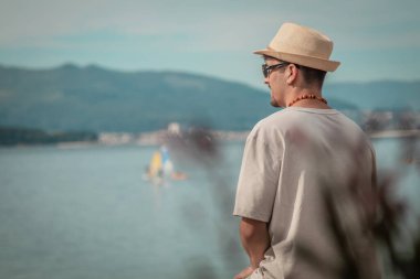 Genç adam sahilde oturmuş denize bakıyor.