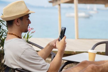Plaj barında cep telefonu kullanan genç bir adam.