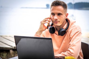 Dizüstü bilgisayarı ve terasta telefonu olan genç bir adam.
