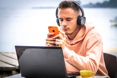 Bilgisayarlı ve dışarıda telefon kullanan genç bir adam.