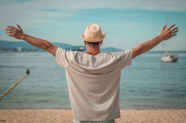 Özgür adam plajda rahatlamış, kolları havada.