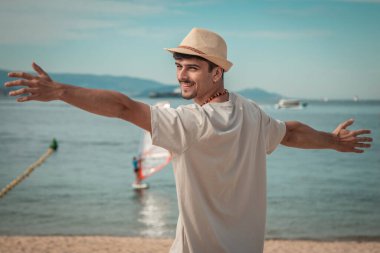 Özgür adam plajda rahatlamış, kolları havada.