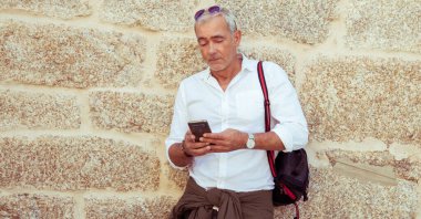 Gülümseyen olgun bir adam sokakta telefonla konuşuyor.