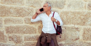 Gülümseyen olgun bir adam sokakta telefonla konuşuyor.