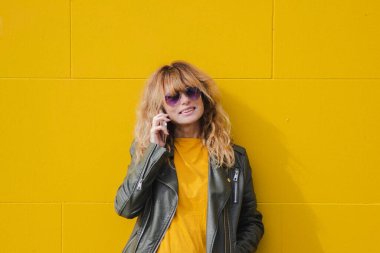 Duvara yaslanmış cep telefonu olan olgun bir kadın.