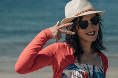 Plajda hasır şapkalı ve güneş gözlüklü genç bir kadının portresi.