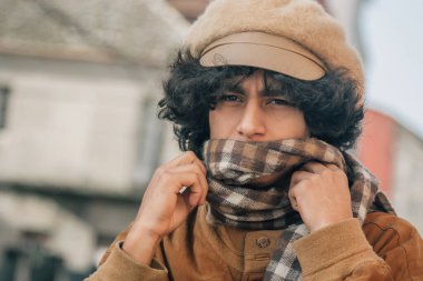 Genç adam kışın sokakta atkıyla ısınıyor.