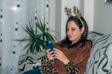 Yılbaşında evde cep telefonu kullanan genç bir kadın.