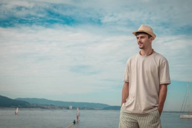 Kumsalda yürüyen şapkalı genç adam.