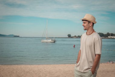 Kumsalda yürüyen şapkalı genç adam.