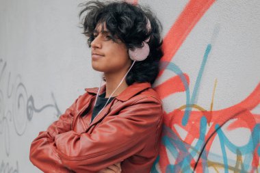 Sokak duvarında kulaklıkları olan Latin kökenli genç bir adam.