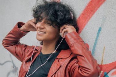 Sokak duvarında kulaklıkları olan Latin kökenli genç bir adam.