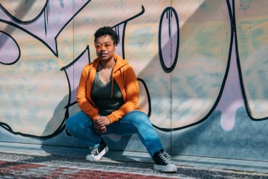 Eşofmanlı Afro-Amerikan kadın grafiti duvarında poz veriyor.