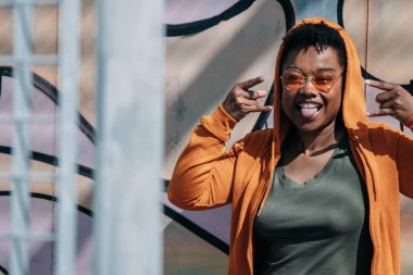 Dilini dışarı çıkaran isyankar hareketlerle genç bir kadın grafiti duvarına poz veriyor.