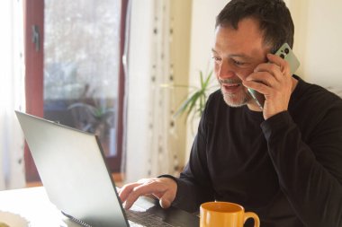 Evde ya da iş yerinde bilgisayar ve telefonla çalışan olgun bir adam