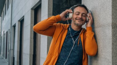Mutlu orta yaşlı adam rahatlamış sokak duvarına yaslanmış müzik dinliyor.