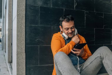 Kulaklıklı dijital tablet kullanan orta yaşlı bir adam.