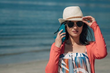 Genç bir kadın sahilde yürüyor ve akıllı telefon kullanıyor.