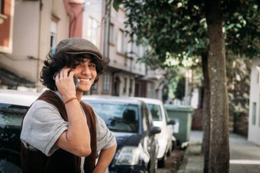 Latin asıllı genç adam gülümsüyor. Cep telefonuyla konuşuyor.