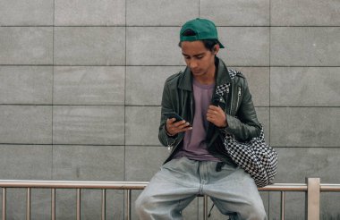 Genç öğrenci şehir caddesinde otururken akıllı telefon kullanarak dışarıda dinleniyor. 