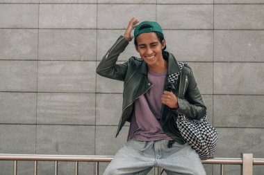 Sırt çantalı genç bir öğrenci sokakta mutlu oturuyor.